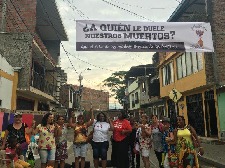 Holmes, Wells and other activist mothers stand before a banner in Colombia that reads, “Who feels for our dead? May the mothers’ pain transcend borders.” PHOTO COURTESY OF GLOBAL NETWORK OF  MOTHERS IN RESISTANCE.